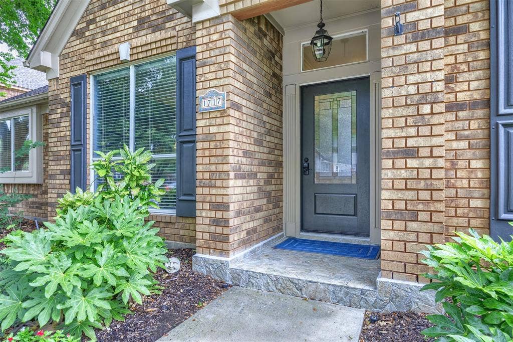1717 Whitney Drive, Richardson, TX 75082 Brick facade featuring a dark entry door with decorative glass, transom window, and a hanging lantern light fixture