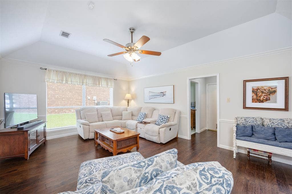 1717 Whitney Drive, Richardson, TX 75082 Spacious living area featuring vaulted ceilings, wood-finish flooring, a ceiling fan with integrated lighting, and crown molding
