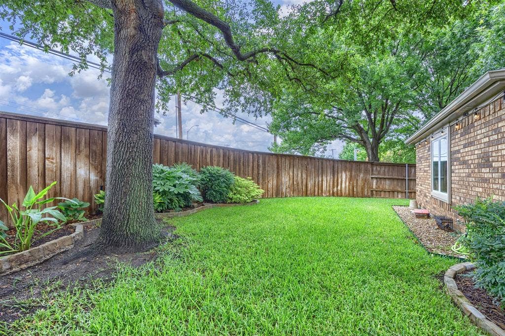 1717 Whitney Drive, Richardson, TX 75082 Spacious backyard featuring a substantial mature tree, lush green lawn, and a wood privacy fence