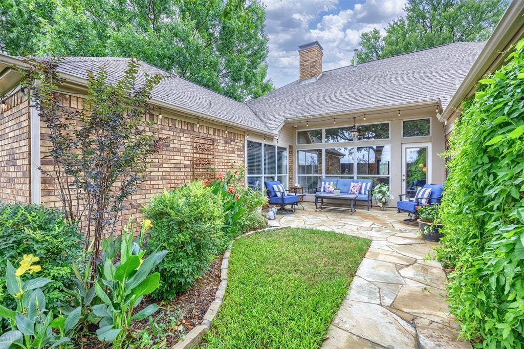 1717 Whitney Drive, Richardson, TX 75082 Flagstone patio with a lush green lawn border, surrounded by mature landscaping and a brick exterior