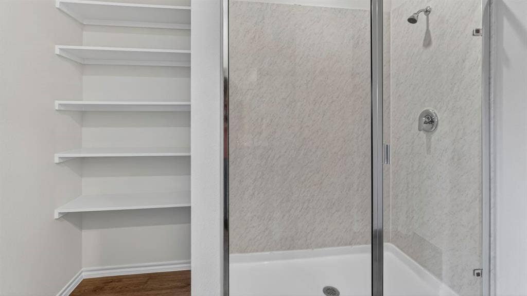 1933 Freeman Street, Tyler, TX 75704 Built-in shelving unit with white shelves, adjacent to a shower enclosure featuring a clear glass door, chrome fixtures, and textured shower surround panels