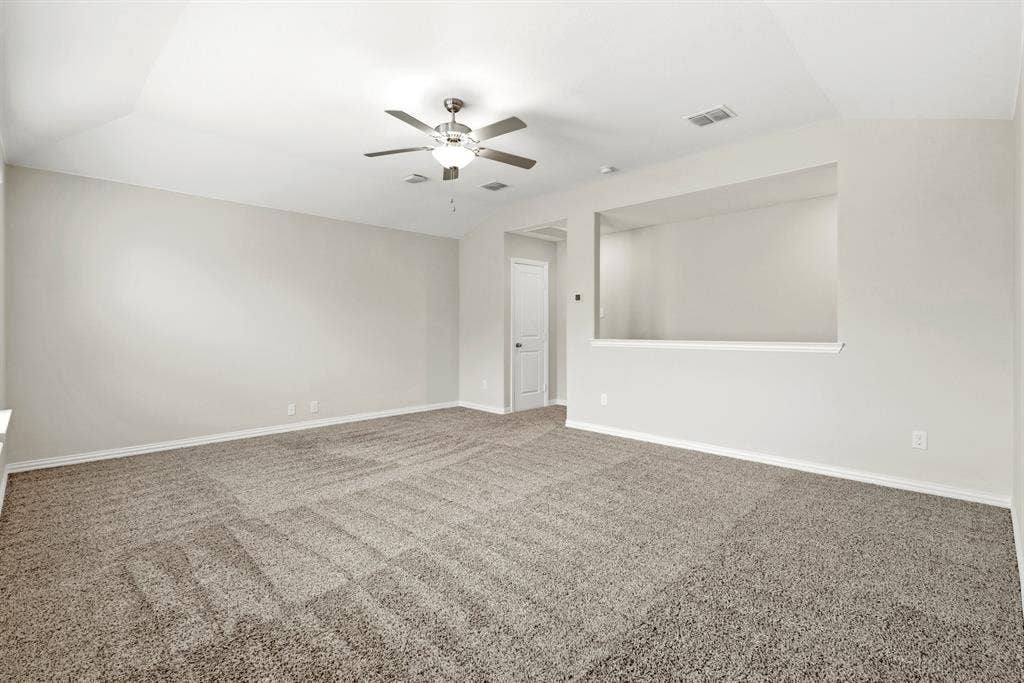 714 Stallings Drive, Princeton, TX 75407 Spacious room featuring vaulted ceilings, a ceiling fan with integrated lighting, soft neutral-toned carpet, and a decorative wall cutout