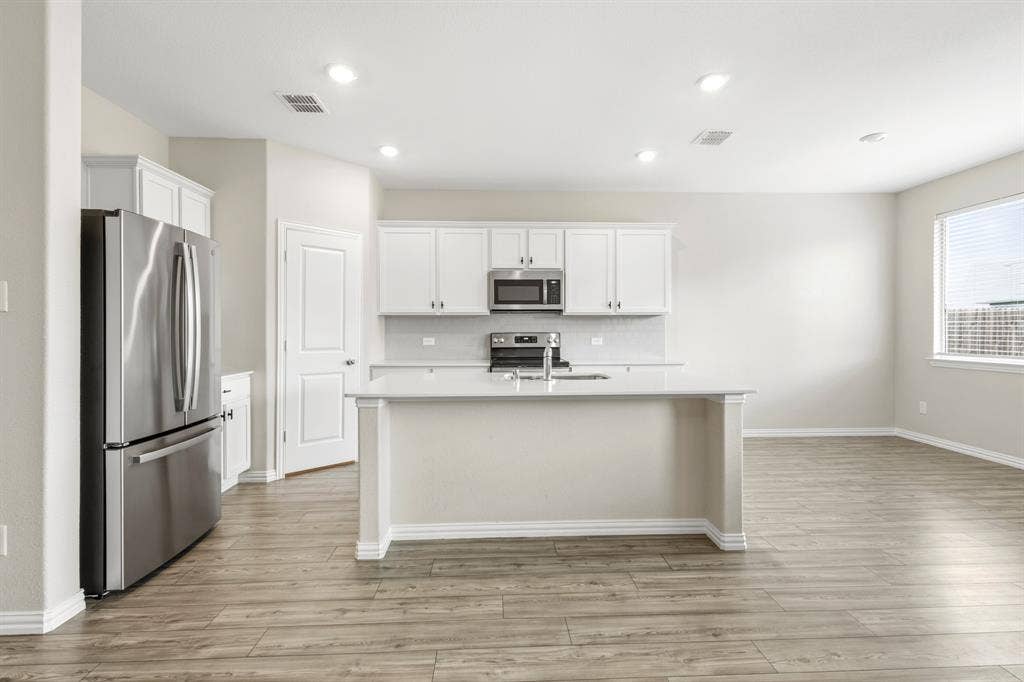 714 Stallings Drive, Princeton, TX 75407 Open-concept kitchen featuring an island with a sink, white cabinetry, stainless steel appliances, and wood-finish flooring