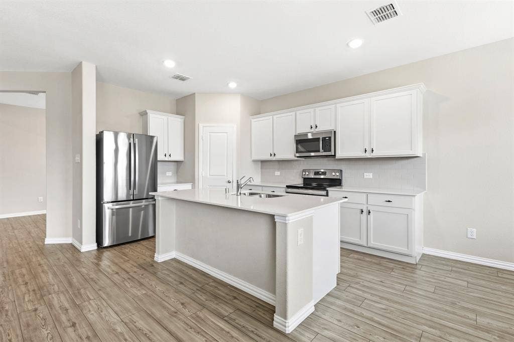 714 Stallings Drive, Princeton, TX 75407 Kitchen featuring white shaker cabinetry, stainless steel appliances, a center island with sink, light-toned countertops, and wood-finish flooring