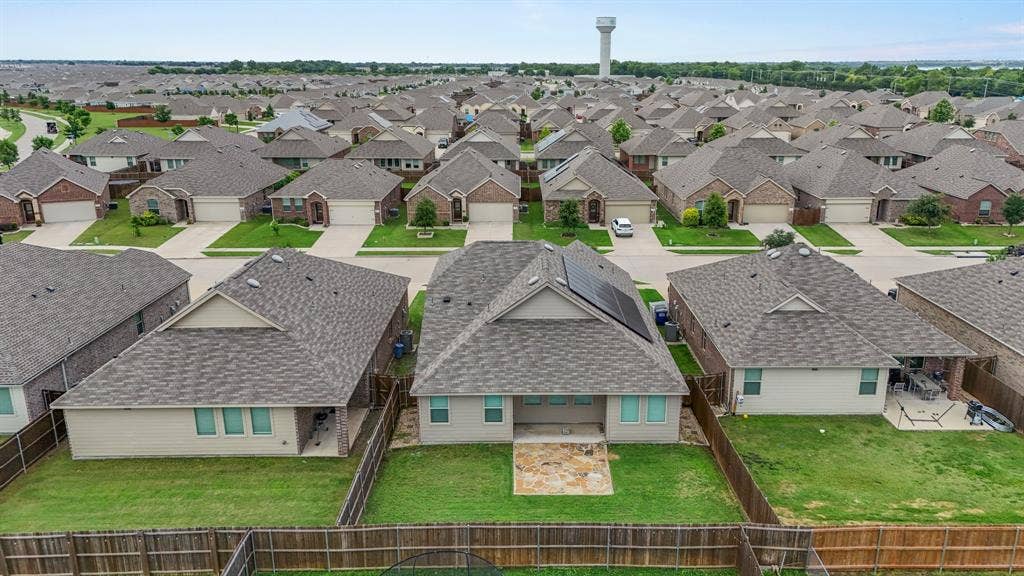 714 Stallings Drive, Princeton, TX 75407 Rear exterior featuring a stone patio, fenced backyard, and multiple roof-mounted solar panels