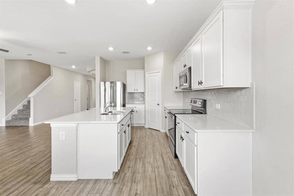714 Stallings Drive, Princeton, TX 75407 Modern kitchen featuring a large central island with double sink, white cabinetry, integrated stainless steel appliances, white countertops, and a tiled backsplash