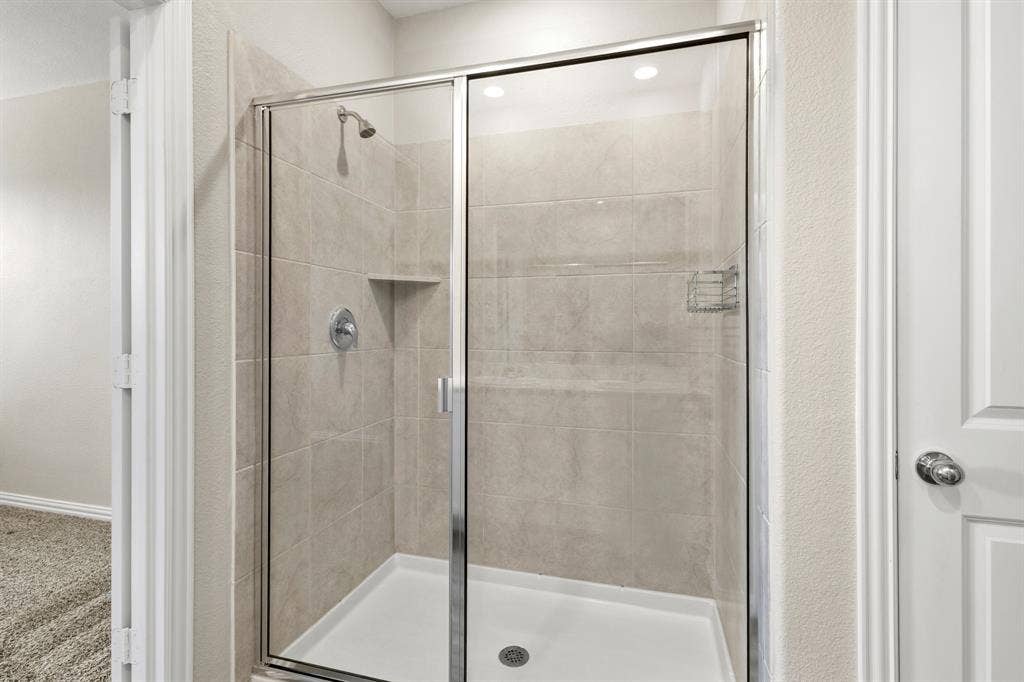 714 Stallings Drive, Princeton, TX 75407 Walk-in shower featuring a chrome-framed glass enclosure, light-toned tile surround, built-in shower niche, and a white shower pan