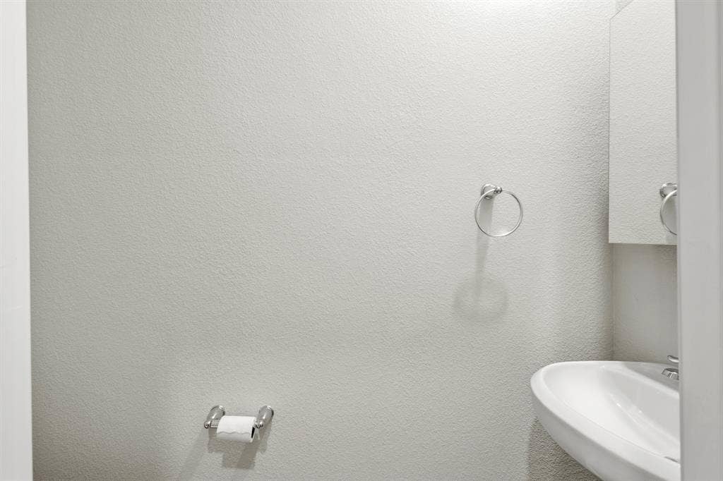 714 Stallings Drive, Princeton, TX 75407 Wall-mounted ceramic sink with chrome faucet, complemented by a mirrored medicine cabinet, chrome towel ring, and chrome toilet paper holder