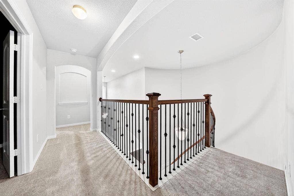 Upper-level hallway featuring a curved wall, recessed lighting, and a chandelier