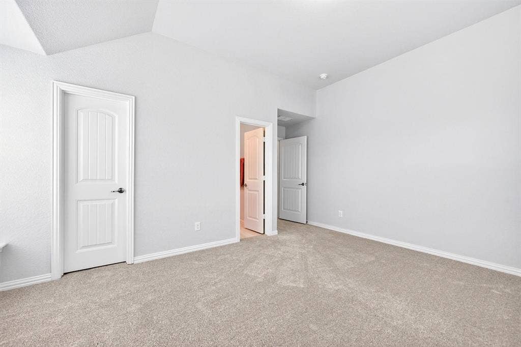 Spacious room featuring vaulted ceilings, light gray wall paint, and plush carpeting