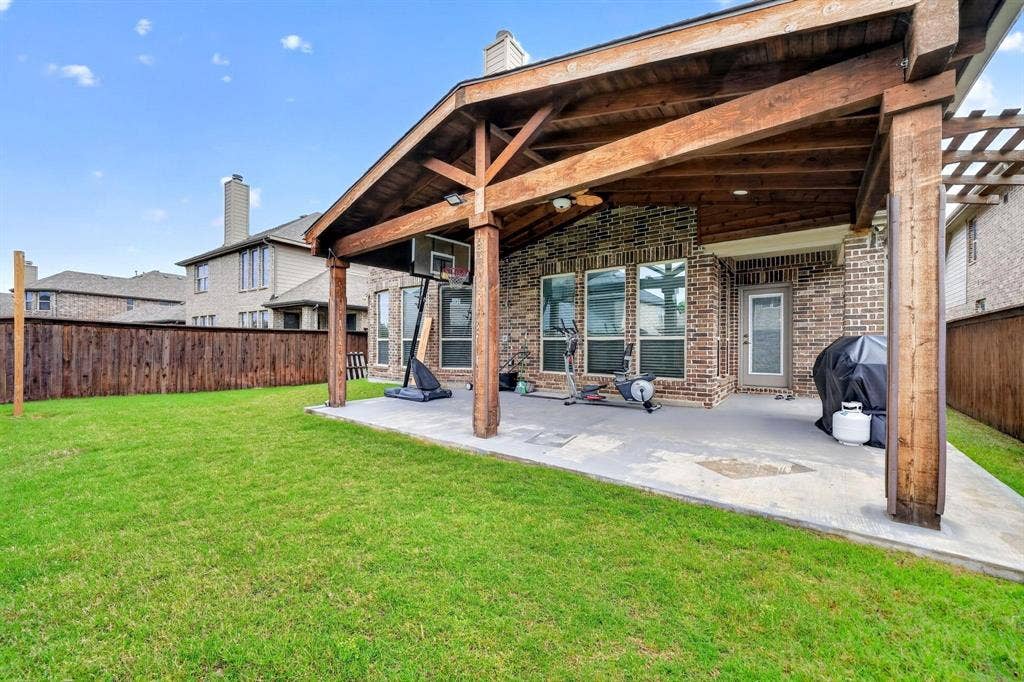Expansive green lawn bordering a covered patio featuring a wood-beam vaulted ceiling, integrated lighting, and a ceiling fan