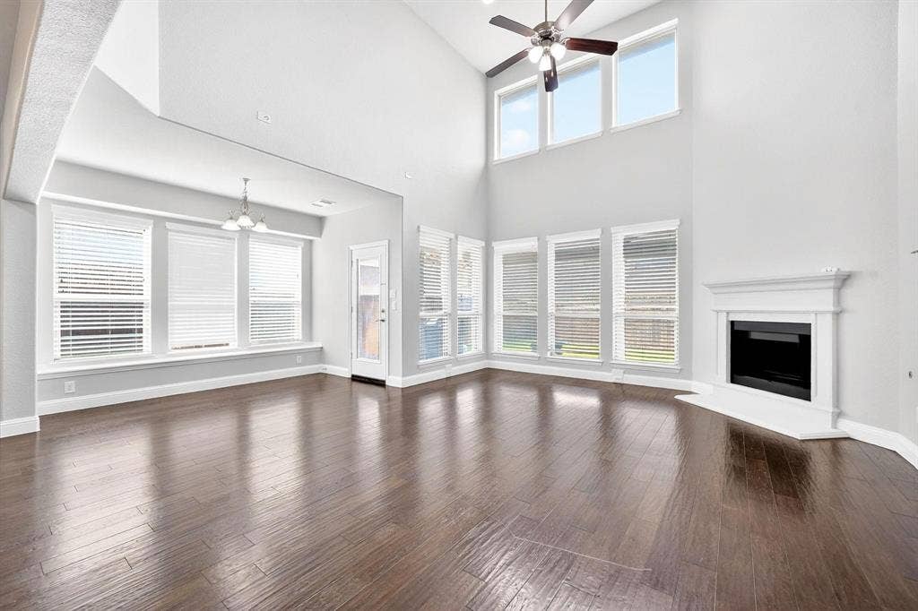 Living area featuring wood-finish flooring, a white mantel fireplace, and a vaulted ceiling with a ceiling fan
