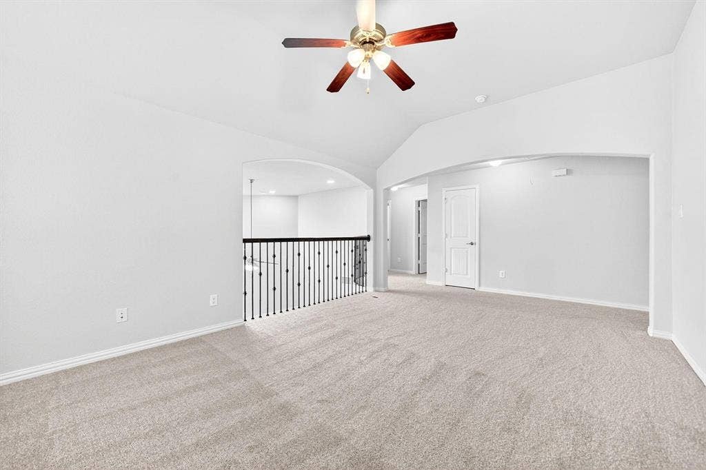 Spacious open area featuring vaulted ceilings with a ceiling fan, plush carpeting, and archway architectural details