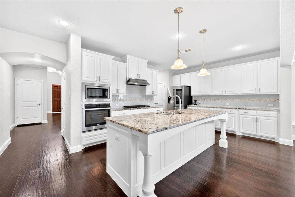 Kitchen featuring a large central island with a stone countertop, white shaker-style cabinetry, stainless steel appliances, dark wood-finish flooring, and recessed lighting