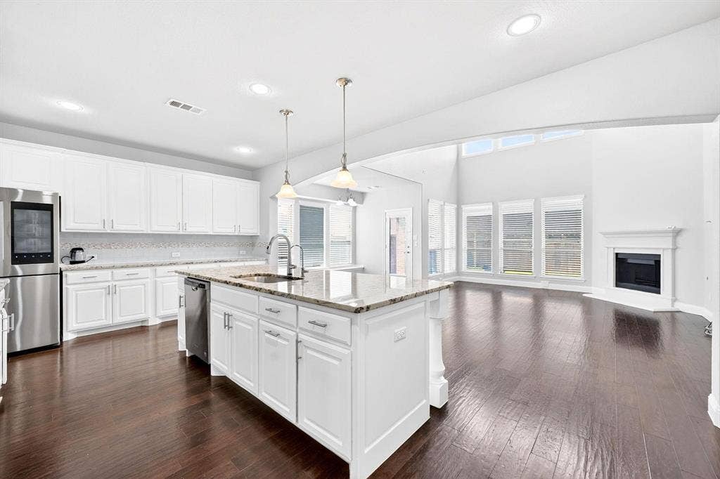 Open-concept kitchen featuring white cabinetry, a large center island with a double basin sink, stainless steel appliances, and wood-finish flooring