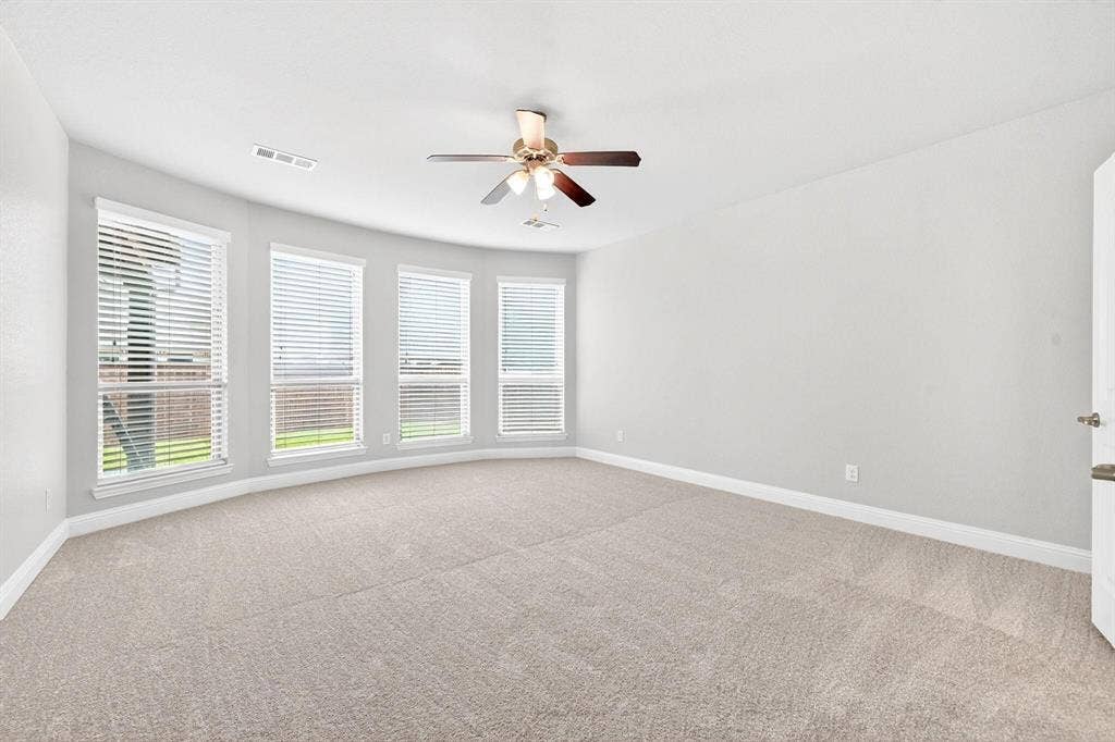 Spacious room featuring a curved bay window with four individual windows, neutral carpet flooring, a ceiling fan, and white baseboards