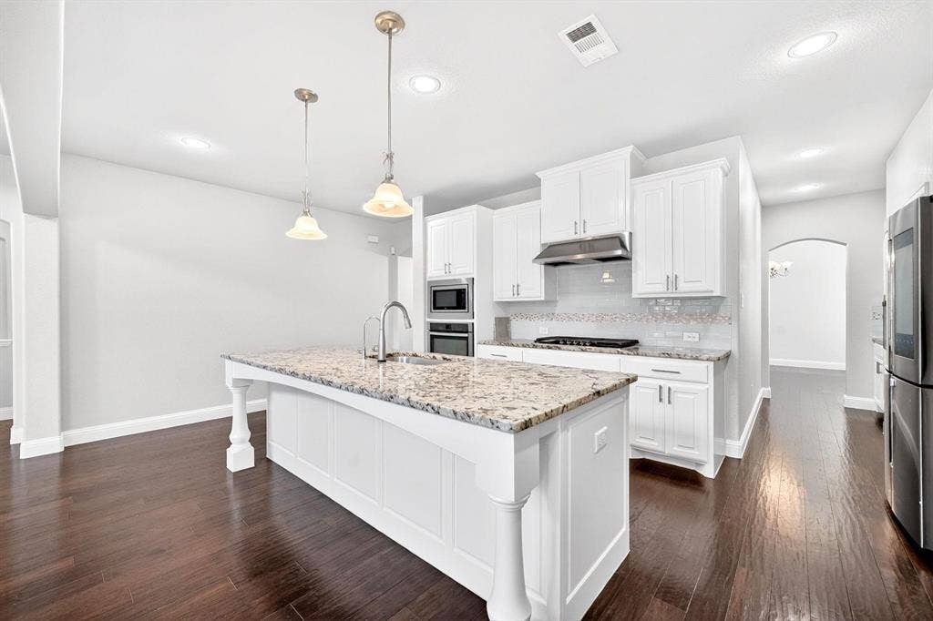 Kitchen featuring a central island with a granite countertop, white cabinetry, stainless steel appliances, and dark wood-finish flooring