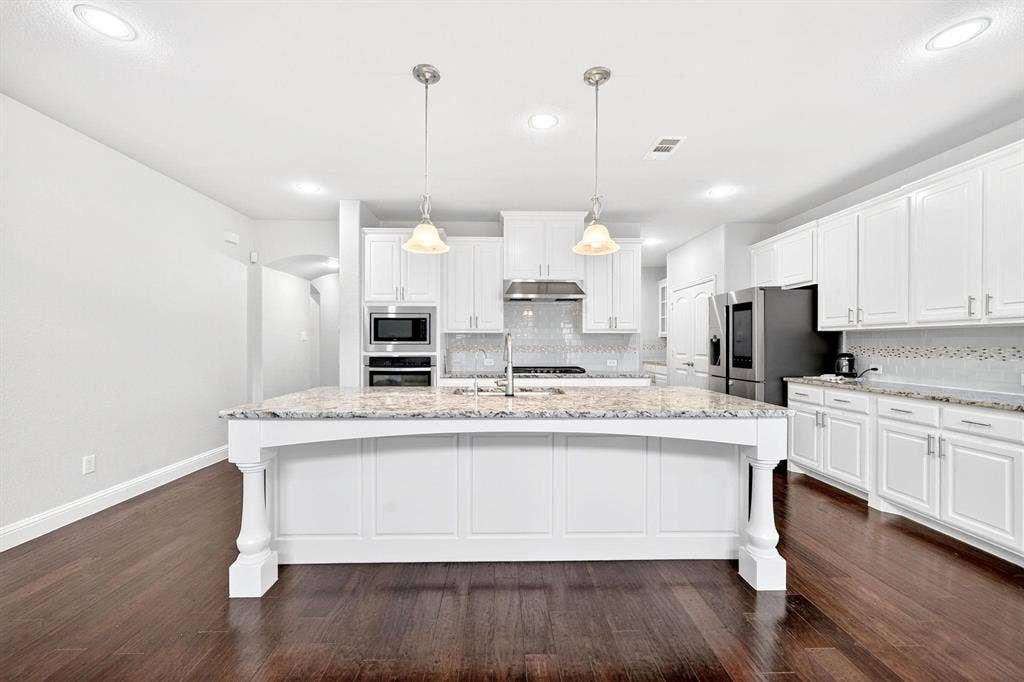 Spacious kitchen featuring an expansive center island with pendant lighting, white cabinetry, dark wood-finish flooring, recessed lighting, and a tiled backsplash