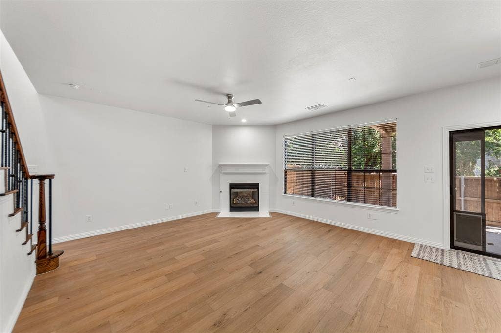 7916 Hannah Street, Plano, TX 75025 Spacious living area featuring wood-finish flooring, a corner fireplace with a white mantel, and a ceiling fan