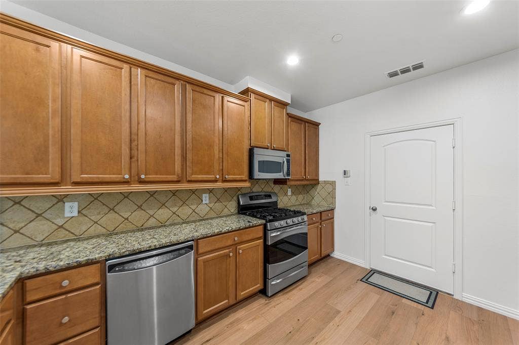 7916 Hannah Street, Plano, TX 75025 Kitchen featuring wood-finish cabinetry, stainless steel appliances, granite countertops, and a decorative tile backsplash