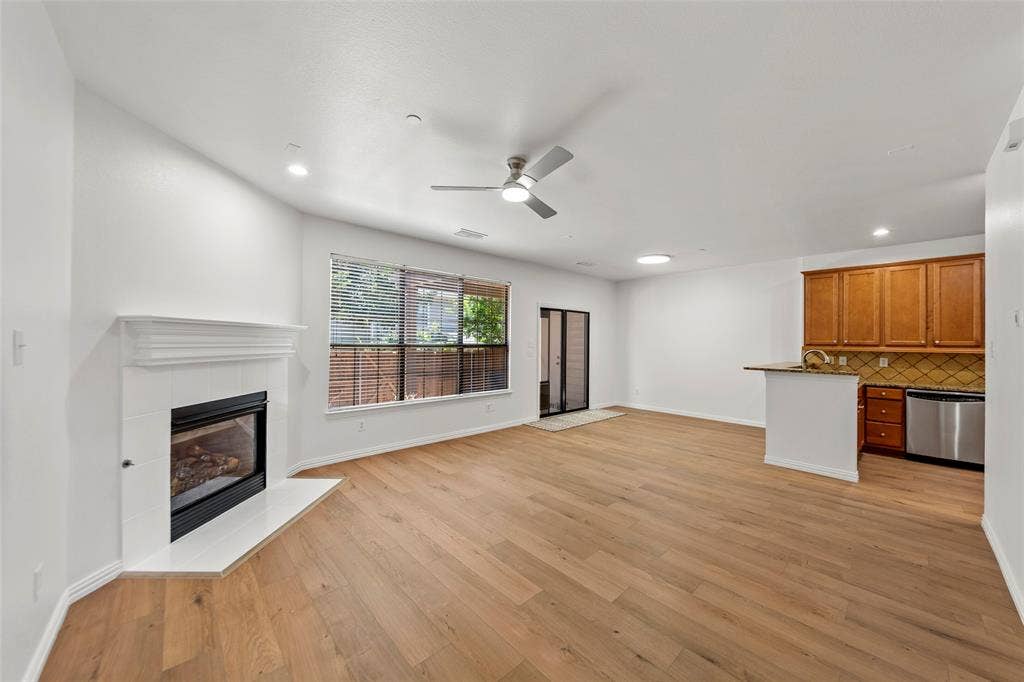7916 Hannah Street, Plano, TX 75025 Open-concept living area featuring wood-finish flooring, a contemporary fireplace with a white mantel, and a kitchen island with seating