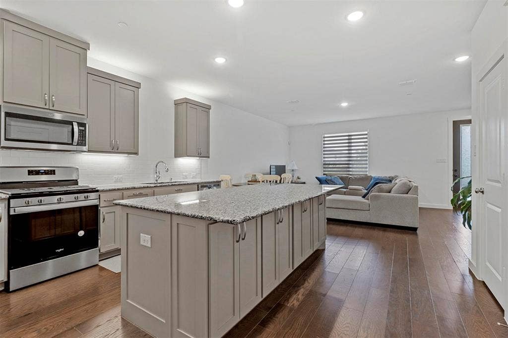 616 Collier Drive, Plano, TX 75075 Kitchen featuring an expansive island with a granite countertop, light gray cabinetry, stainless steel appliances, and wood-finish flooring