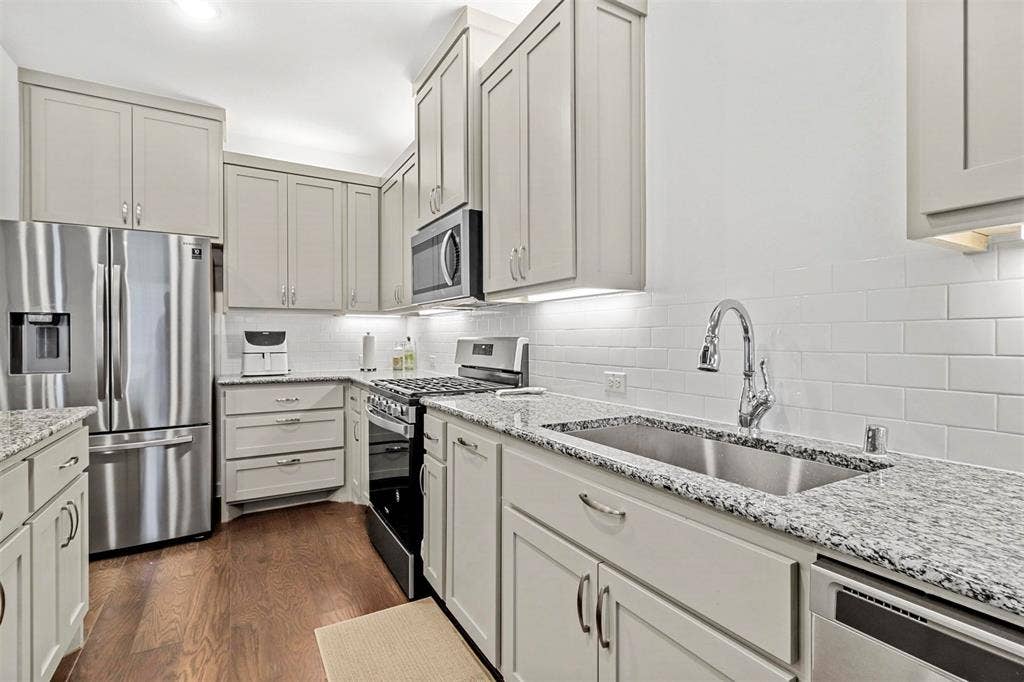 616 Collier Drive, Plano, TX 75075 Modern kitchen featuring light cabinetry, granite countertops, subway tile backsplash, stainless steel appliances, and wood-finish flooring