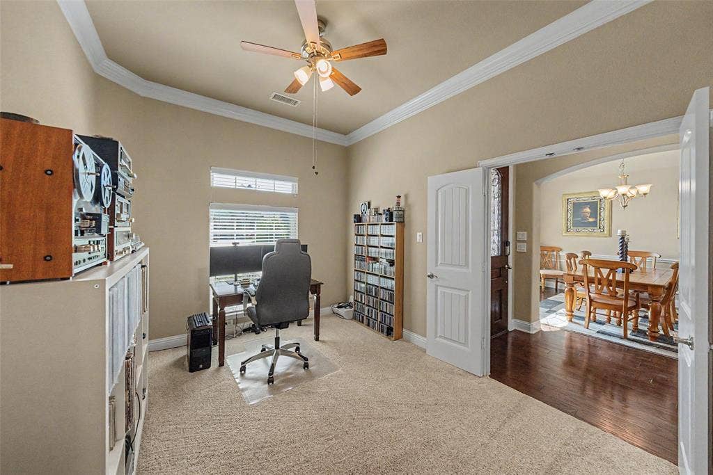 Carpeted room with a ceiling fan, crown molding, and an arched entryway featuring wood-finish flooring