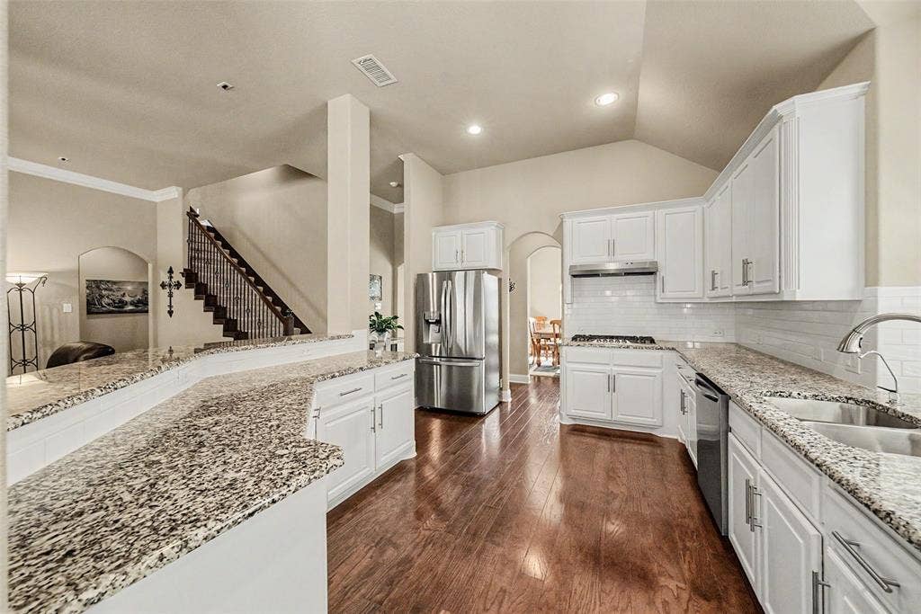 Spacious kitchen featuring wood-finish flooring, white cabinetry, granite countertops, and stainless steel appliances