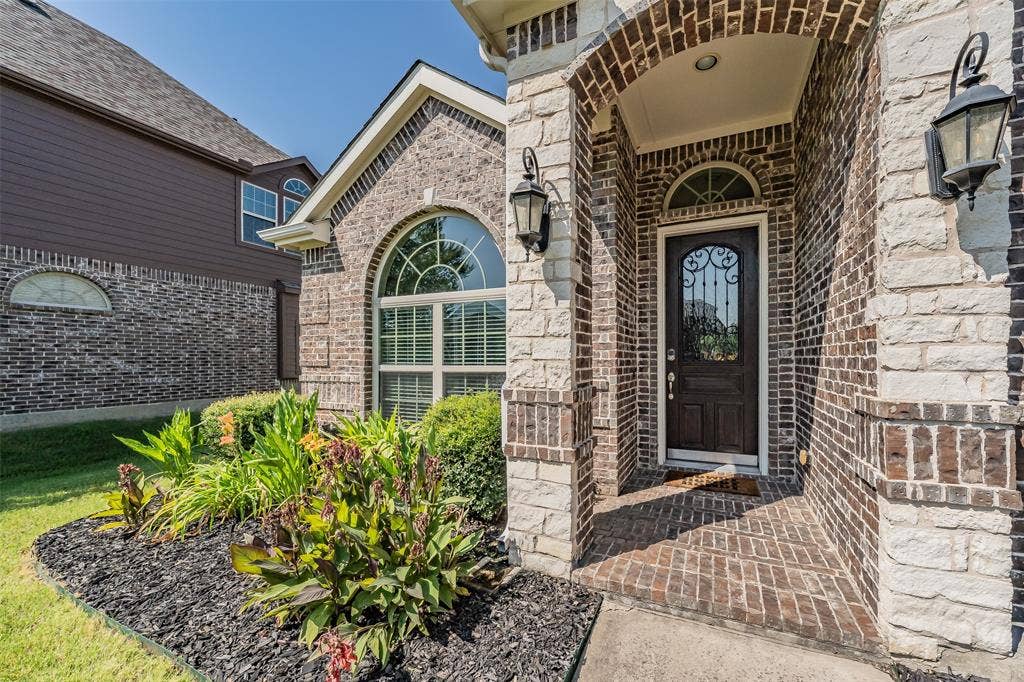 Brick and stone facade featuring an arched entryway, decorative glass front door, and two exterior lanterns