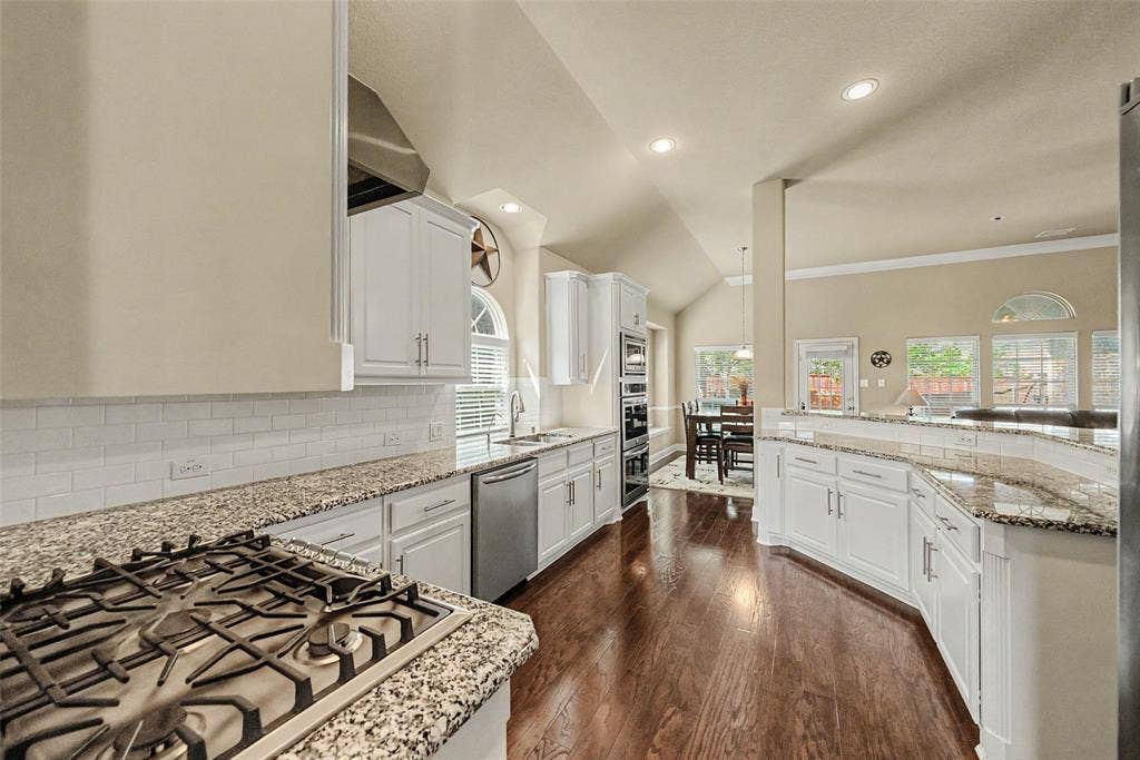Kitchen featuring white cabinetry, granite countertops, wood-finish flooring, stainless steel appliances, and a subway tile backsplash