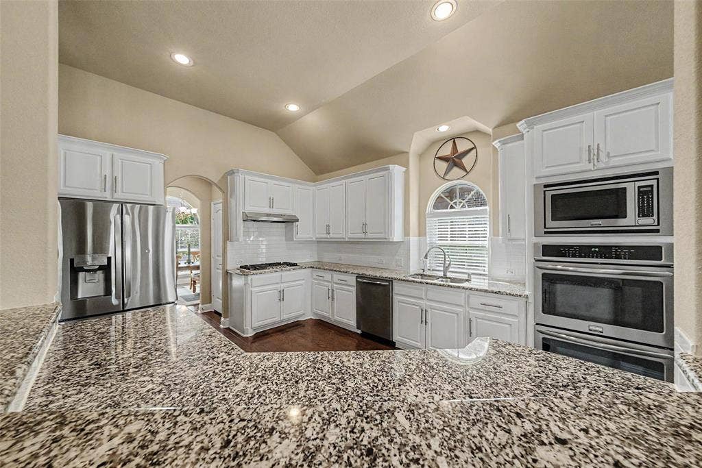 Kitchen featuring white cabinetry with brushed nickel hardware, speckled granite countertops, and a subway tile backsplash