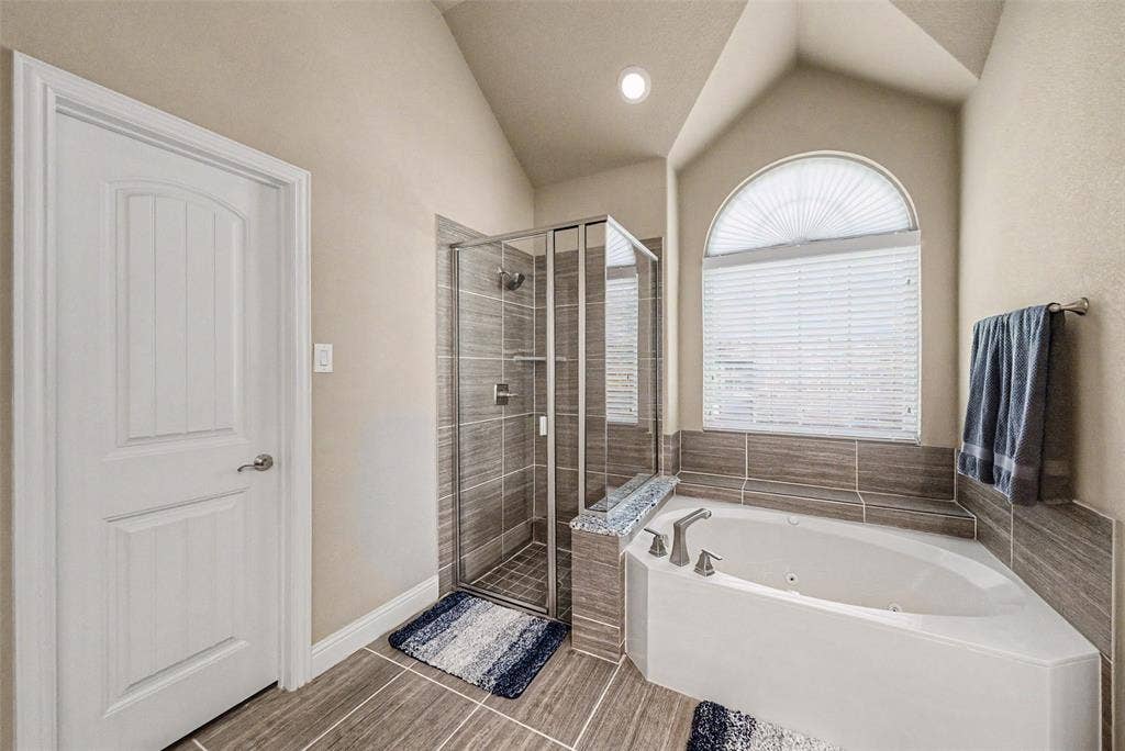 Bathroom featuring a corner soaking tub with deck-mounted fixtures, an arched window with horizontal blinds, and a tiled shower enclosure with a glass door