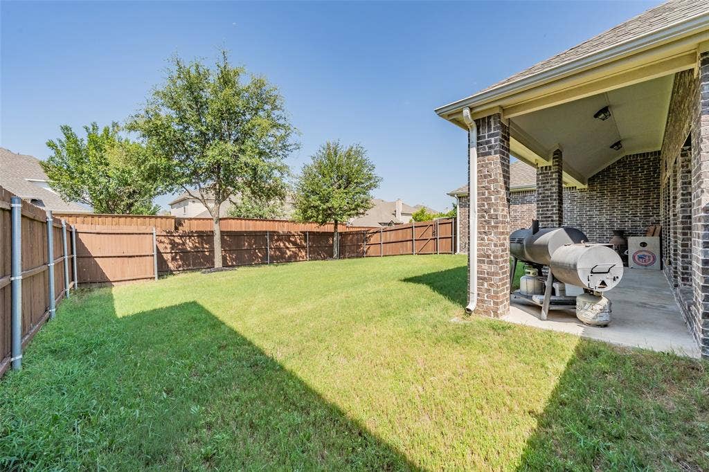 Expansive backyard featuring a lush lawn and a covered patio with brick columns