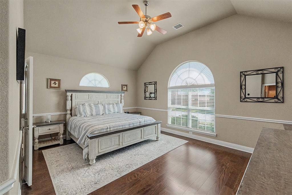 Vaulted ceiling room featuring rich wood-finish flooring, a ceiling fan with light fixture, and arched windows providing natural illumination