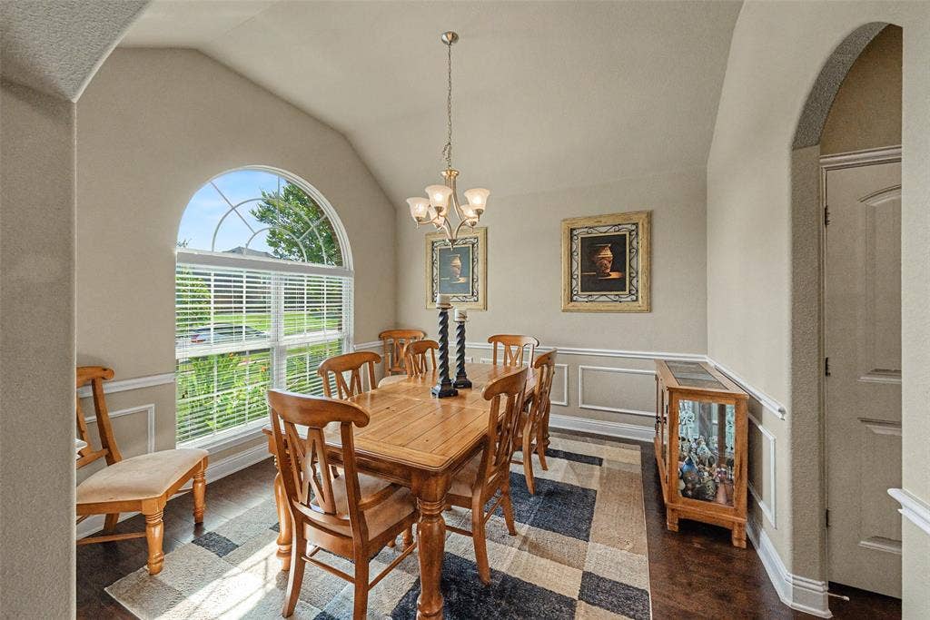 Dining area featuring a vaulted ceiling with a chandelier, an arched window, wood-finish flooring, wainscoting, and an arched entry