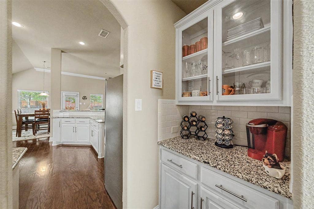 Kitchen featuring white cabinetry, granite-style countertops, subway tile backsplash, and glass-front upper cabinets