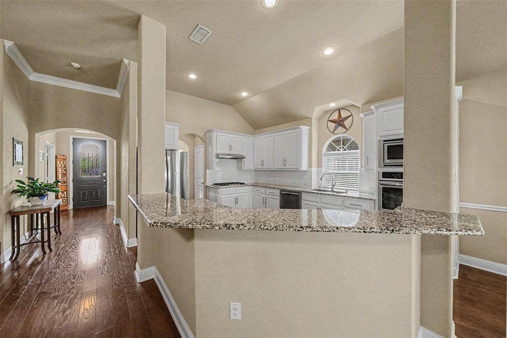 Modern kitchen featuring white cabinetry, a granite countertop island, stainless steel appliances, and a tile backsplash