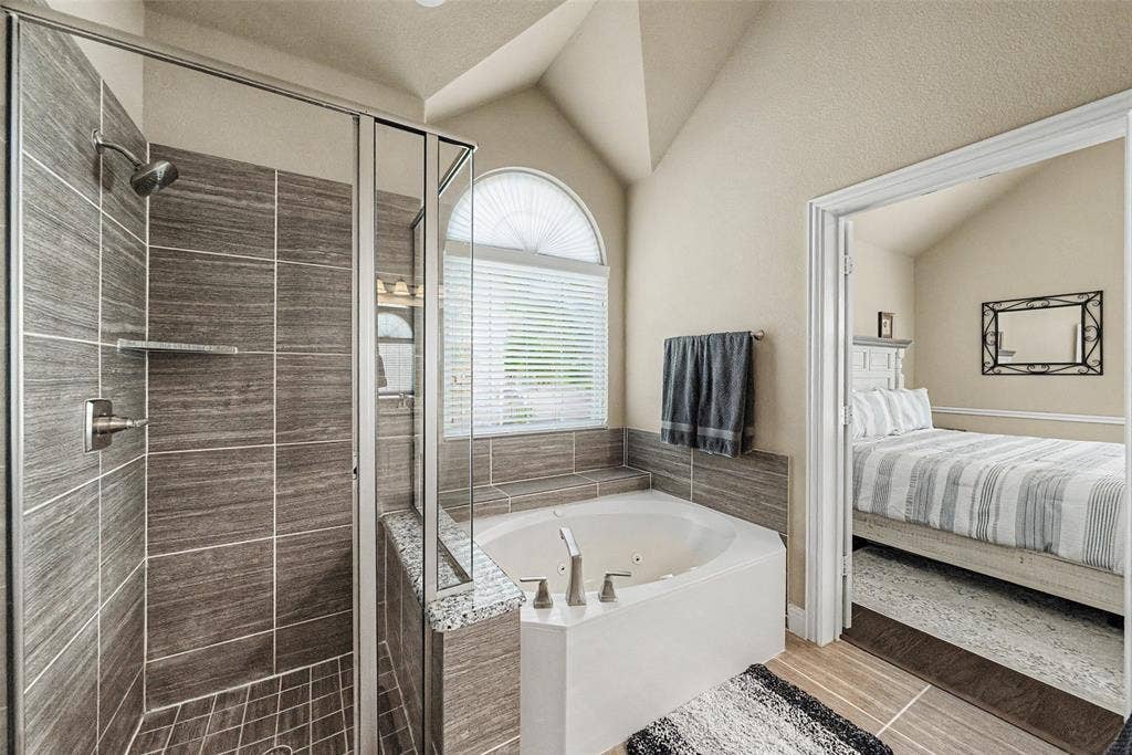 Spacious bathroom featuring a glass-enclosed shower with horizontal tile surround and a built-in corner bathtub with an arched window