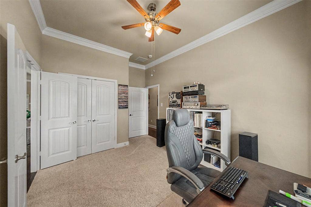 Carpeted interior room featuring crown molding, neutral wall color, and a ceiling fan with integrated lighting
