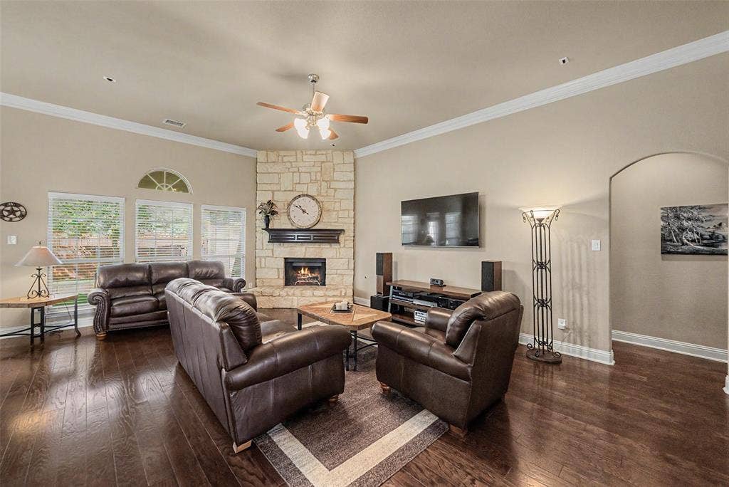 Spacious living room featuring rich wood-finish flooring, a stone fireplace with a dark mantel, and multiple windows with an arched transom
