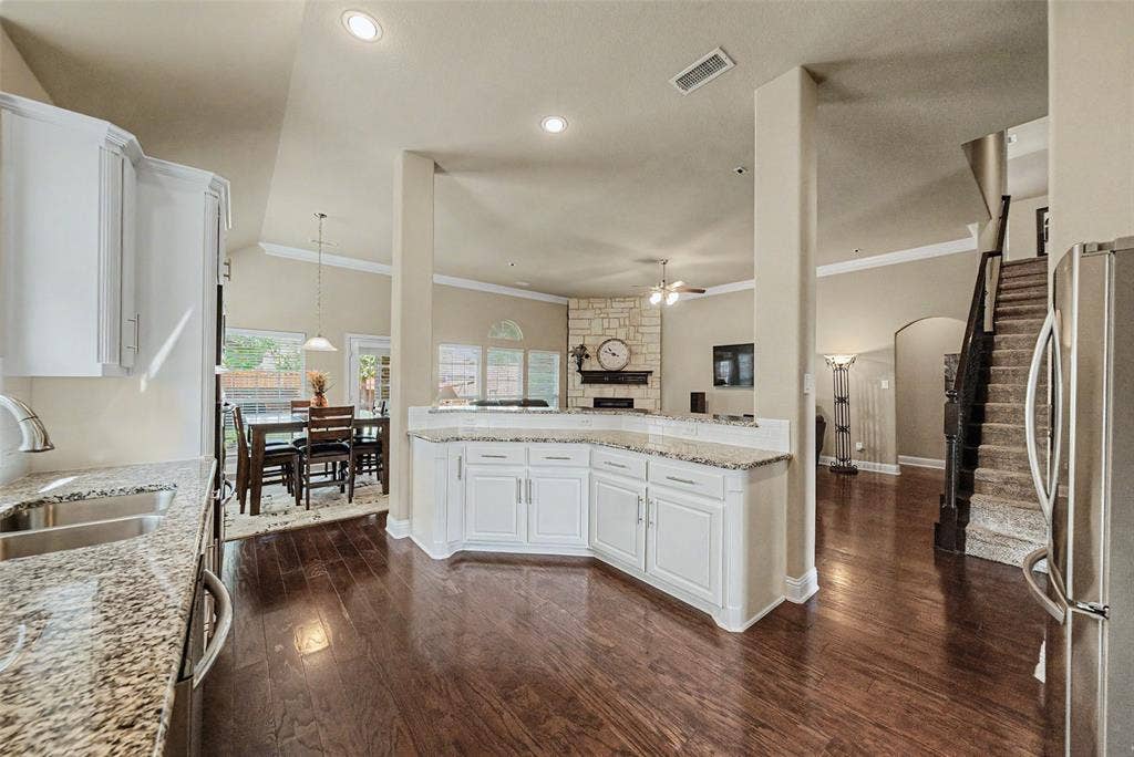 Open-concept interior featuring wood-finish flooring, white cabinetry, granite countertops, and recessed lighting