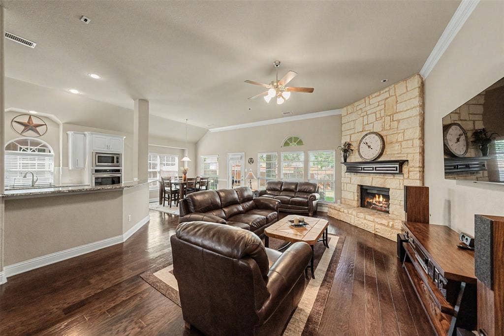 Spacious living area featuring wood-finish flooring, a stone fireplace with hearth and mantel, and vaulted ceilings