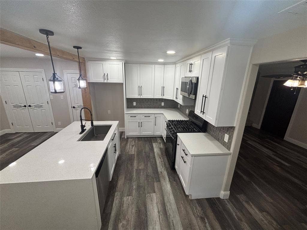 910 NE 31st, Grand Prairie, TX 75050 Modern kitchen featuring white cabinetry with matte black hardware, quartz countertops, stainless steel appliances including a built-in microwave and gas range, and wood-finish flooring