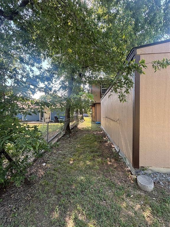 910 NE 31st, Grand Prairie, TX 75050 Expansive side yard featuring a chain-link fence, mature trees, and a beige exterior structure with brown trim