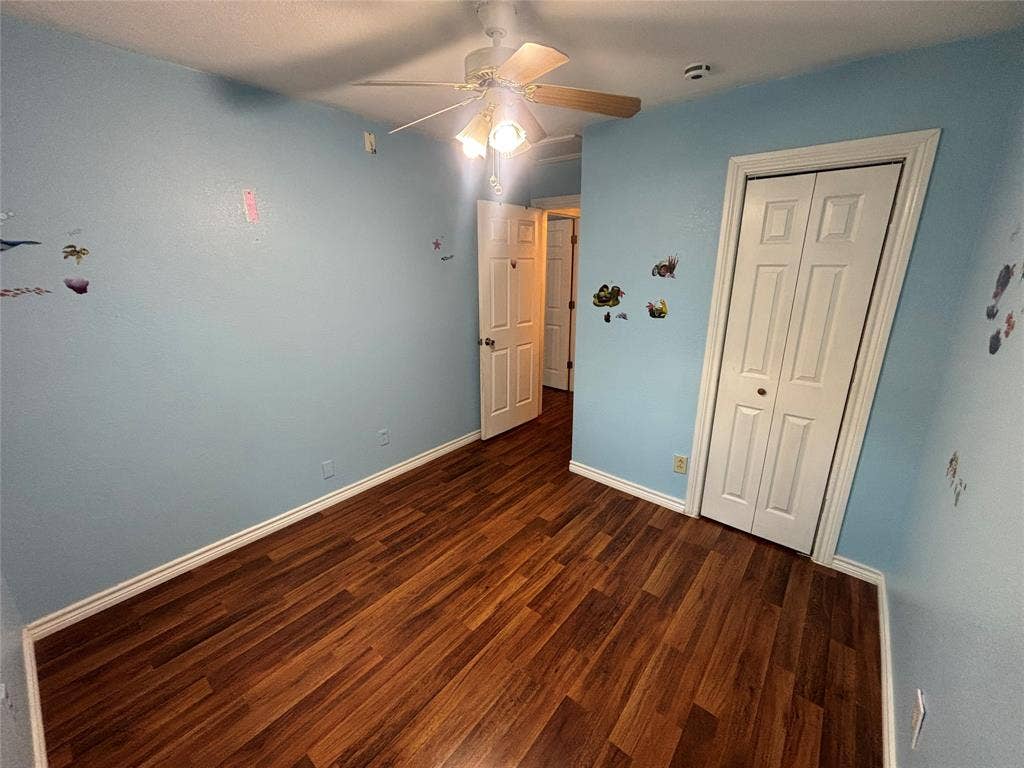910 NE 31st, Grand Prairie, TX 75050 Interior room featuring wood-finish flooring, white baseboards, a ceiling fan with light fixture, and a white bi-fold closet door