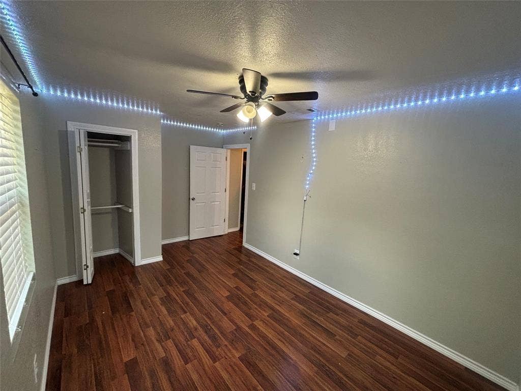 910 NE 31st, Grand Prairie, TX 75050 Room featuring wood-finish flooring, a ceiling fan with integrated lighting, a built-in closet with double doors, and a window with horizontal blinds