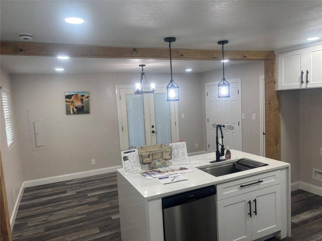 910 NE 31st, Grand Prairie, TX 75050 Kitchen island featuring a stainless steel sink, white shaker cabinetry with black hardware, and an integrated dishwasher