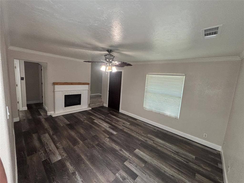 910 NE 31st, Grand Prairie, TX 75050 Living area featuring wood-finish flooring, a white mantel fireplace with a wood top, a ceiling fan, crown molding, and a window with blinds