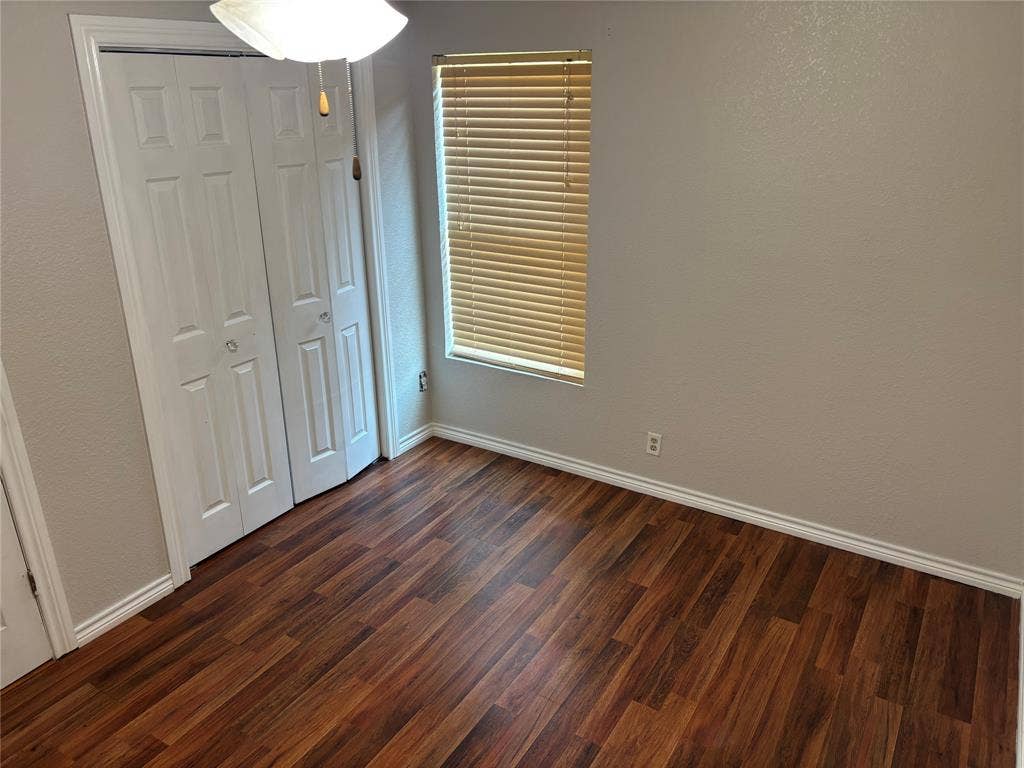 910 NE 31st, Grand Prairie, TX 75050 Interior room featuring wood-finish flooring, light neutral-toned walls, and a window with horizontal blinds